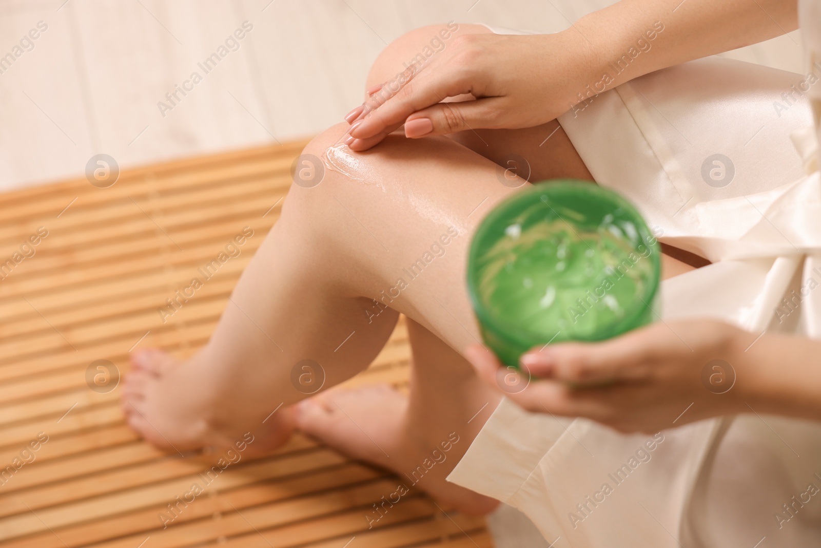 Photo of Young woman applying aloe gel onto leg indoors, closeup