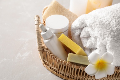 Photo of Wicker tray with fresh towel, plumeria flower and toiletries on light table, closeup. Spa treatment