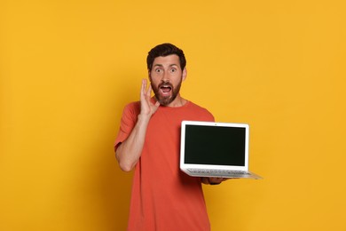 Emotional man with laptop on orange background