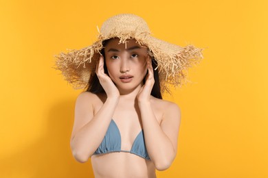 Beautiful young woman in straw hat on orange background