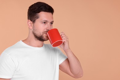 Photo of Man drinking from red mug on beige background. Space for text