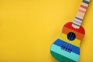 Photo of Colorful ukulele on yellow background, top view with space for text. String musical instrument