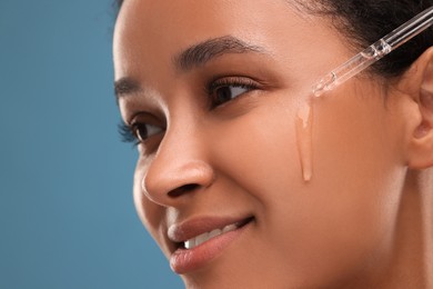 Photo of Smiling woman applying serum onto her face on blue background, closeup
