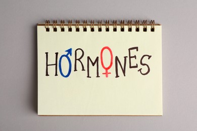 Photo of Notebook with word HORMONES on grey background, top view