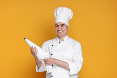 Photo of Portrait of happy confectioner in uniform holding piping bag on orange background