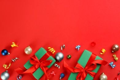Colorful serpentine streamers, Christmas balls and gift boxes on red background, flat lay. Space for text