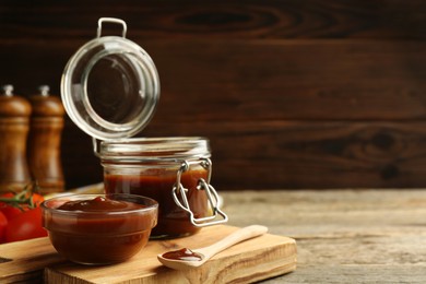 Photo of Tasty barbeque sauce in bowl, jar and spoon on wooden table, closeup. Space for text