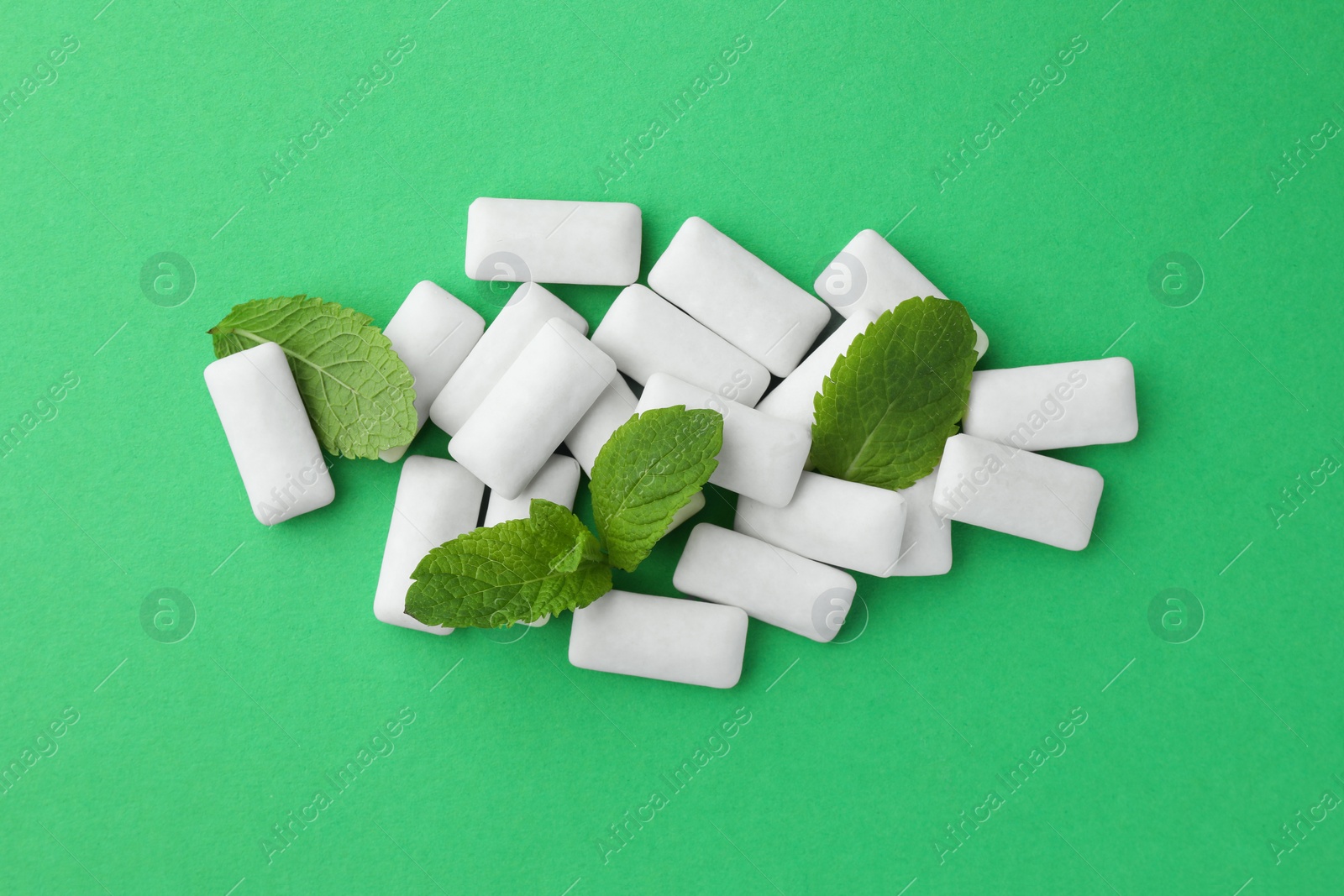 Photo of Tasty white chewing gums and mint leaves on green background, top view