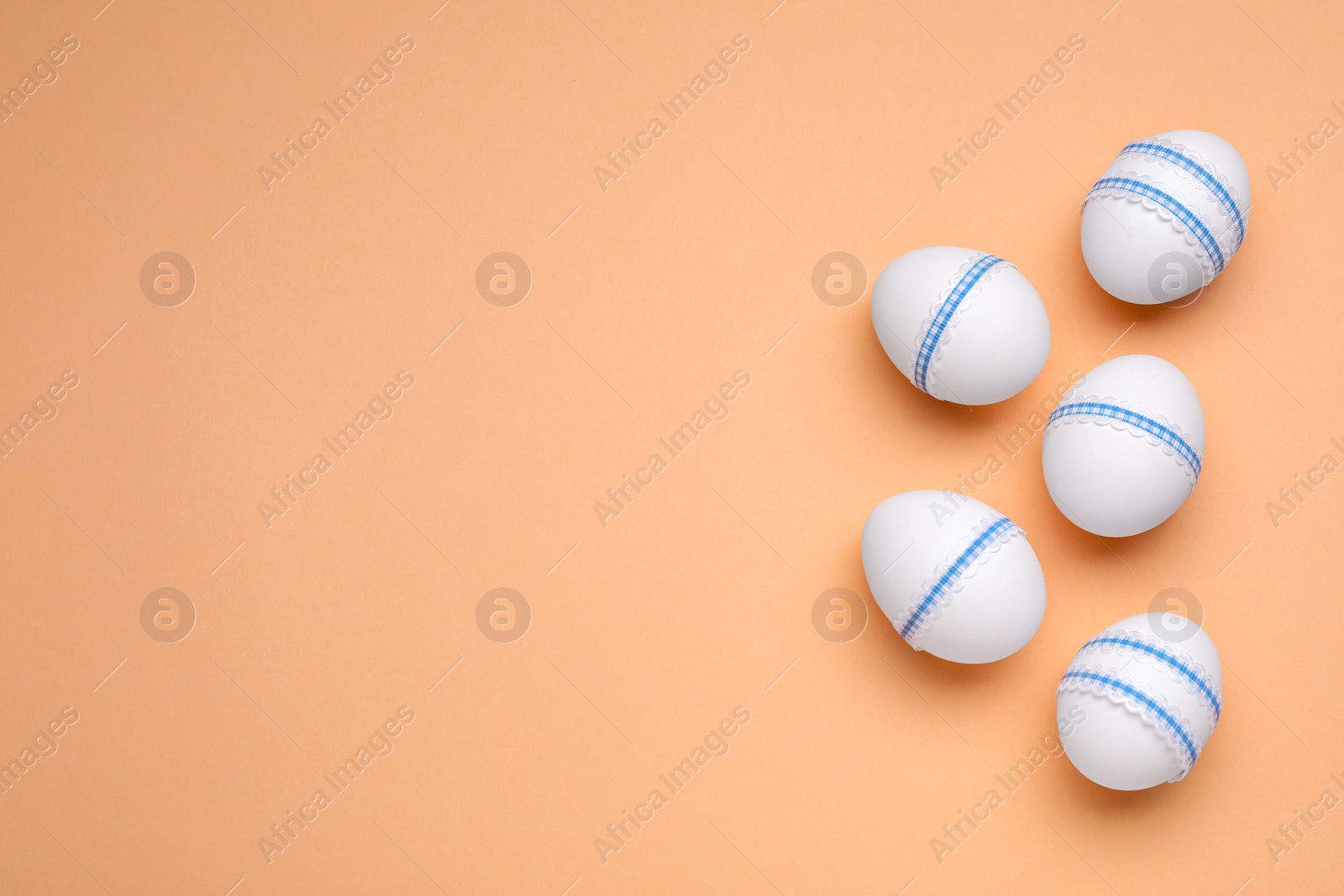 Photo of Beautifully decorated Easter eggs on pale orange background, flat lay. Space for text