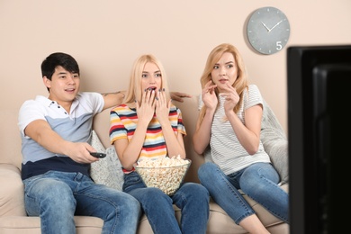 Photo of Young friends with bowl of popcorn watching TV on sofa at home