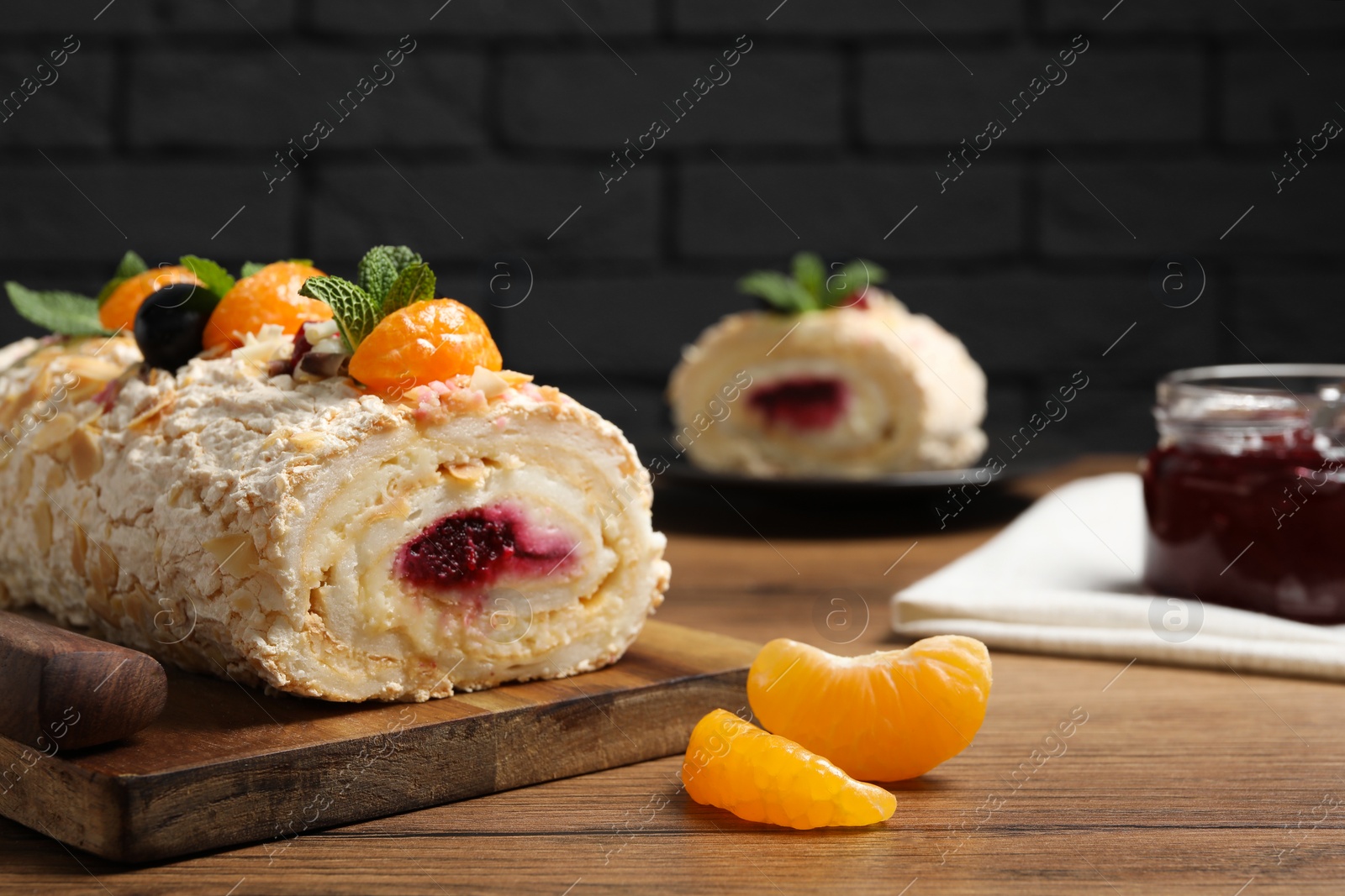 Photo of Tasty meringue roll with jam, tangerine slices and mint leaves on wooden table, closeup. Space for text