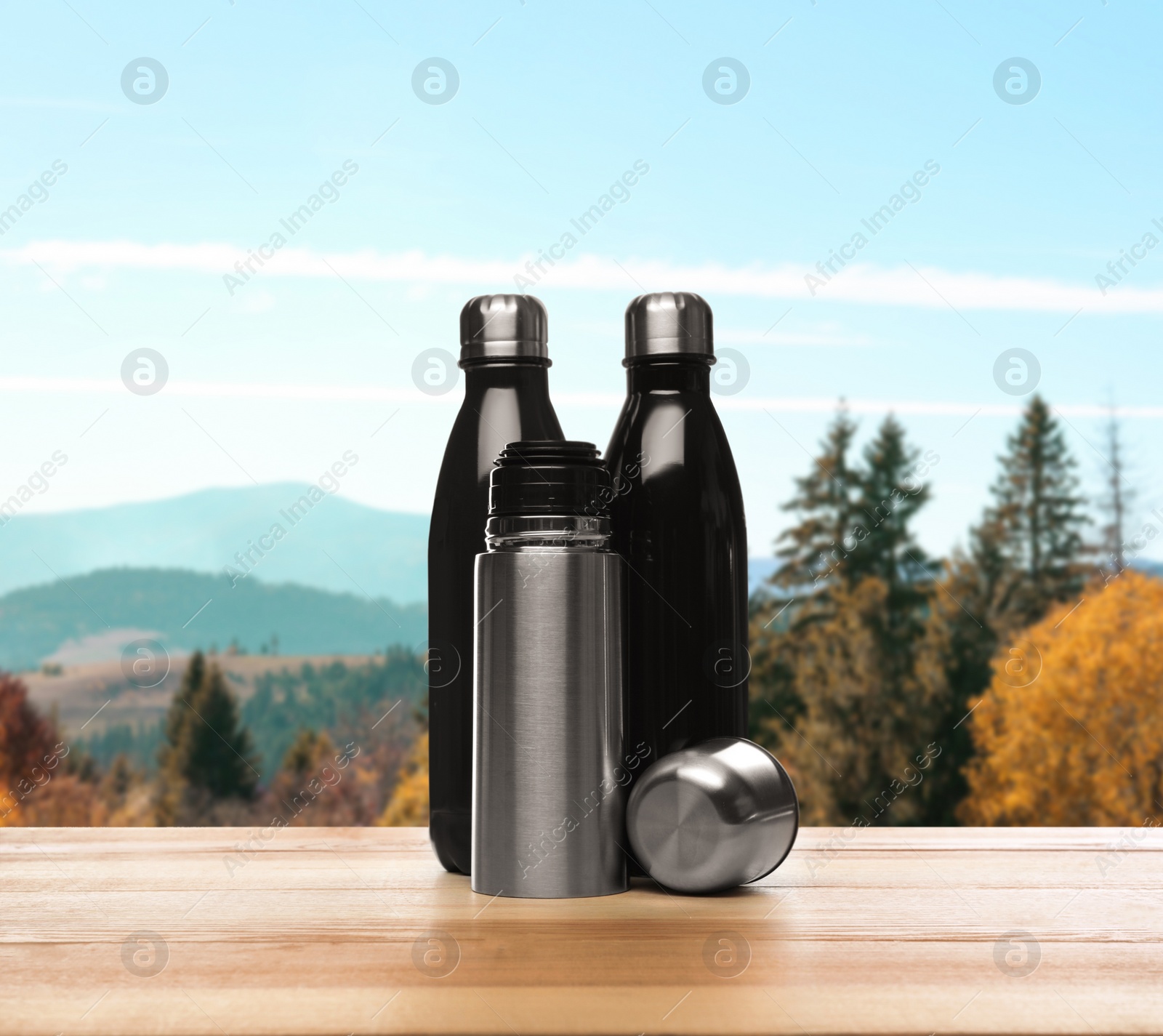 Image of Thermos bottles on wooden table against blurred mountain landscape