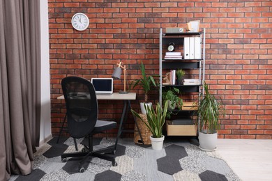 Stylish workplace with desk, chair, bookcase and potted plants at home