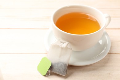 Photo of Tea bag and cup of hot beverage on light wooden table, closeup. Space for text