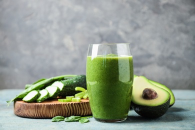 Photo of Delicious green juice and fresh ingredients on light blue wooden table against grey background