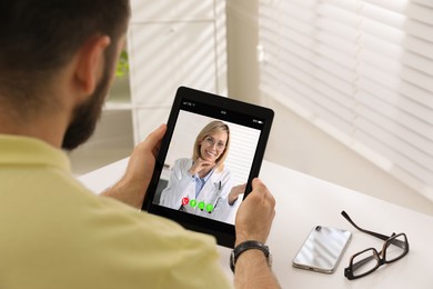 Online medical consultation. Man having video chat with doctor via tablet at table indoors, closeup
