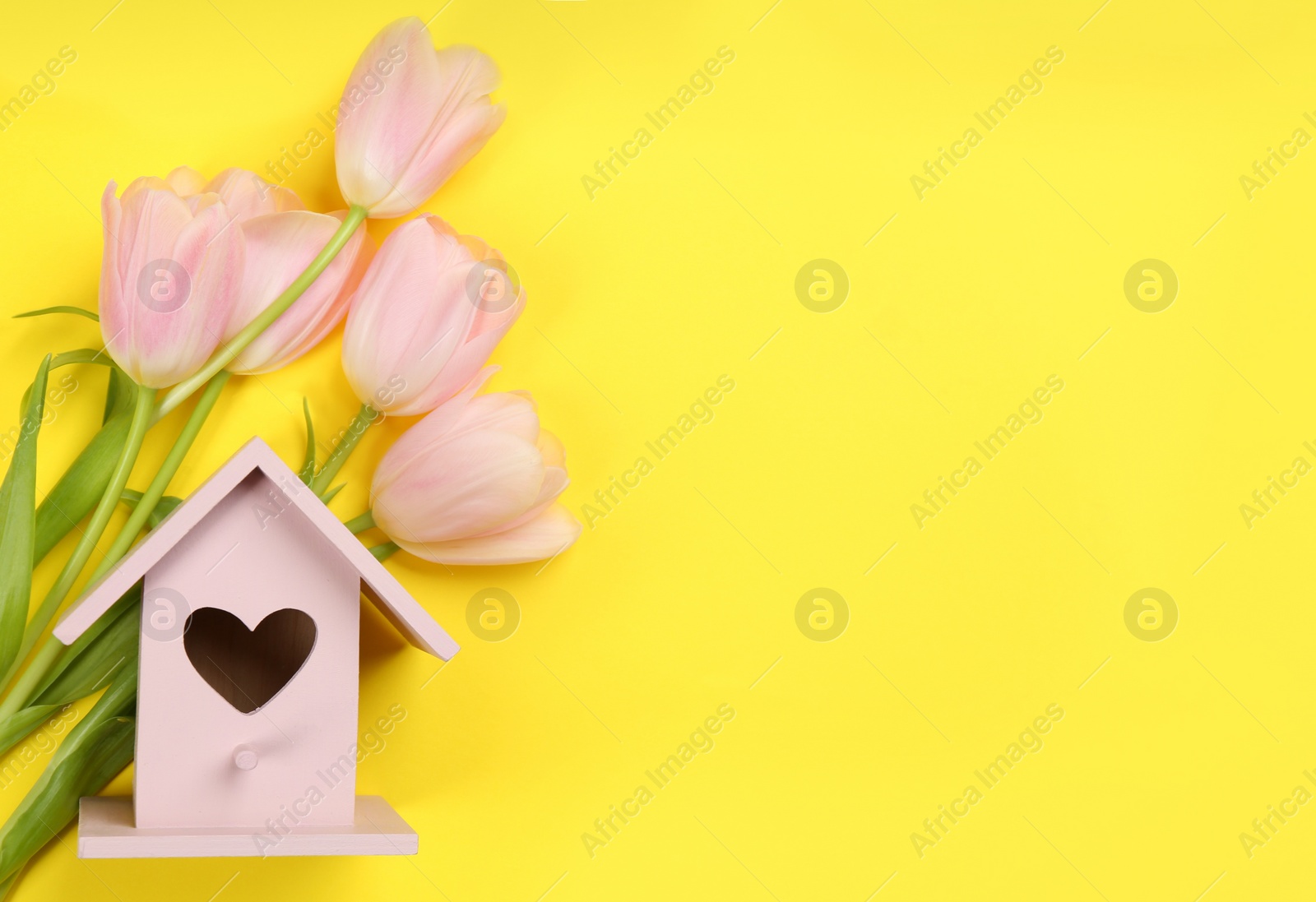 Photo of Beautiful bird house and pink tulips on yellow background, flat lay