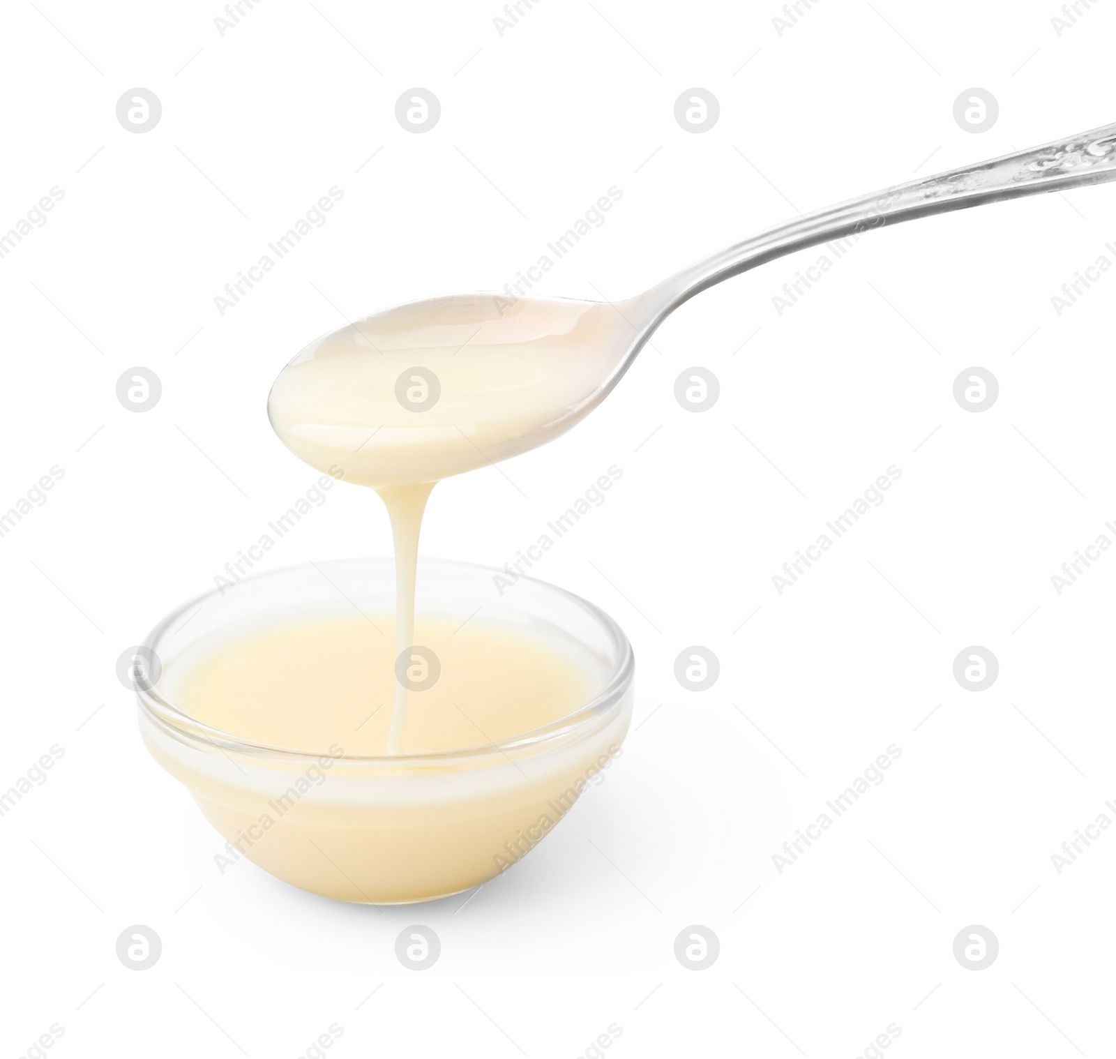 Photo of Condensed milk flowing down from spoon into bowl isolated on white