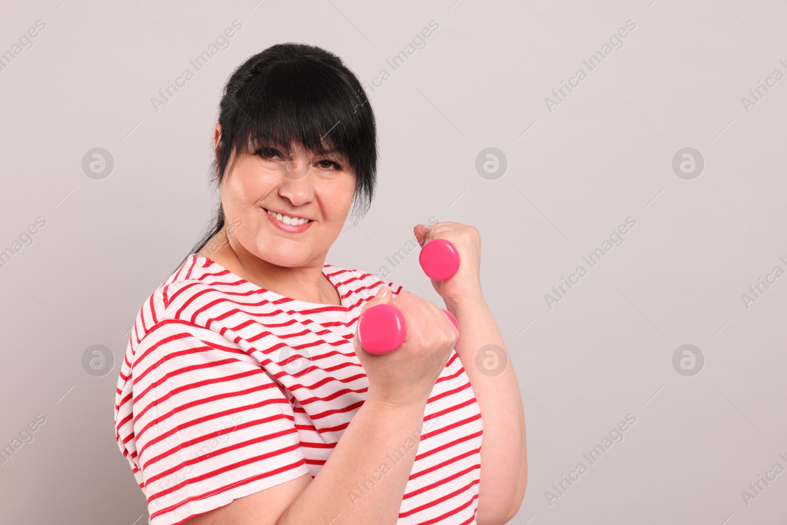 Photo of Happy overweight mature woman doing exercise with dumbbells on grey background. Space for text