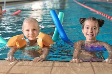 Photo of Little girls with swimming noodles in indoor pool
