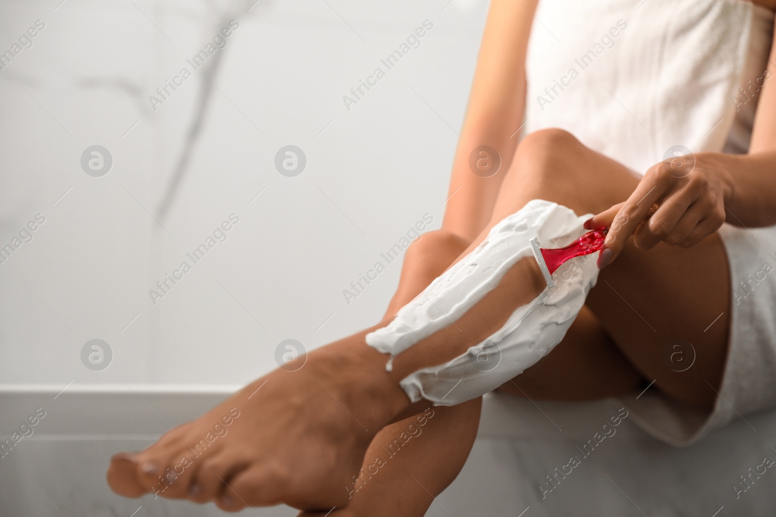 Photo of Beautiful young woman shaving legs in bathroom, closeup