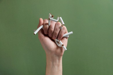 Photo of Stop smoking. Man holding broken cigarettes on olive background, closeup