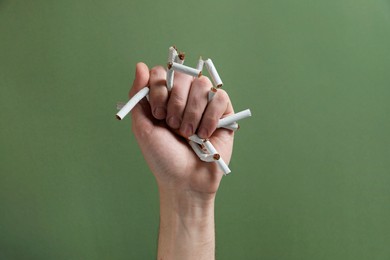 Stop smoking. Man holding broken cigarettes on olive background, closeup