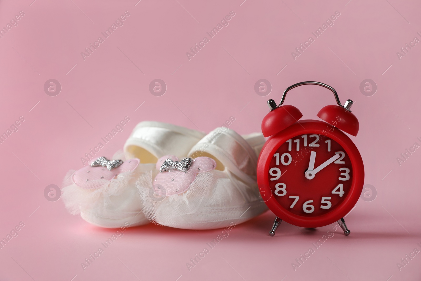 Photo of Alarm clock and baby booties on pink background. Time to give birth