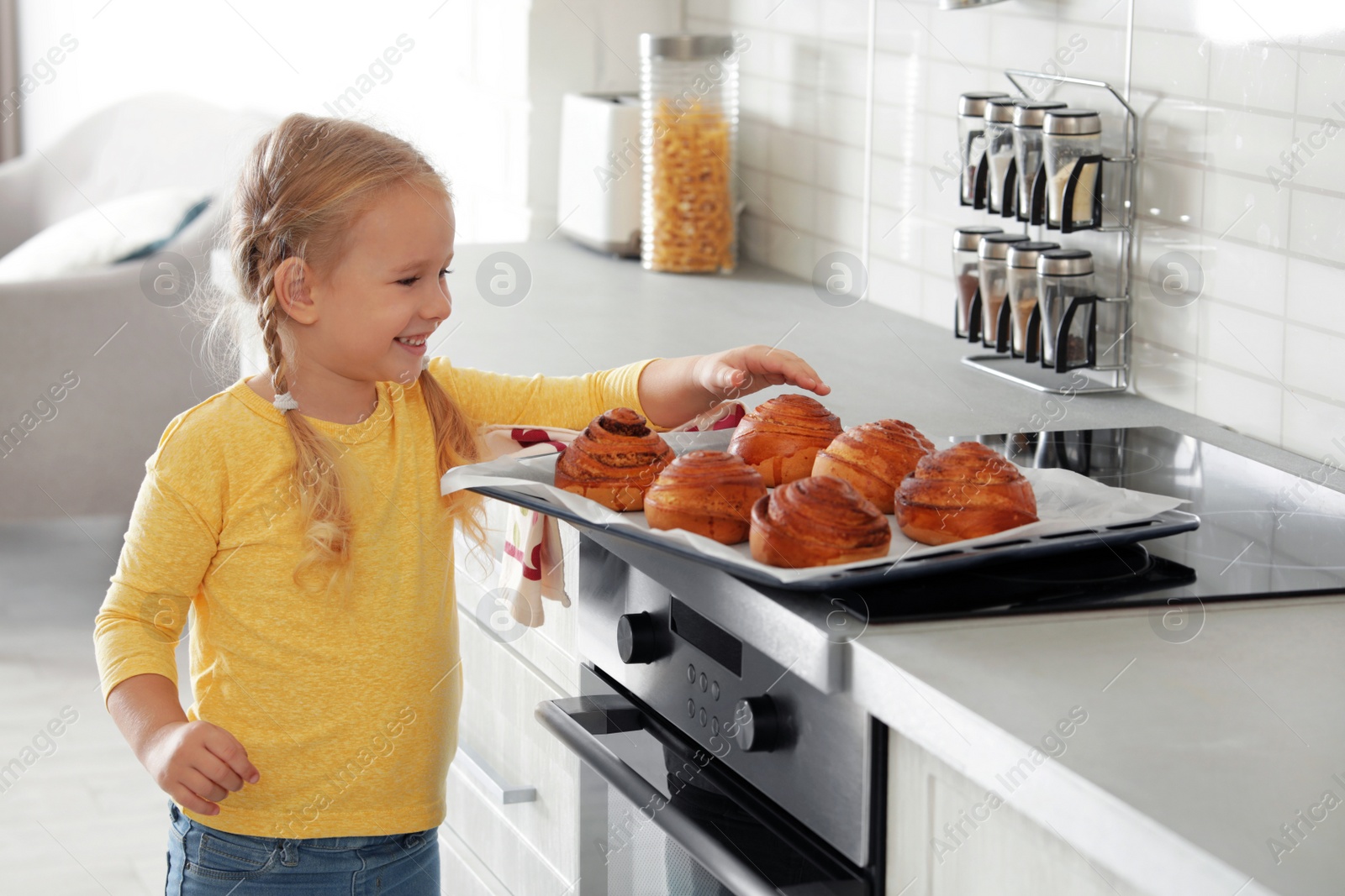 Photo of Little girl with tray of oven baked buns in kitchen