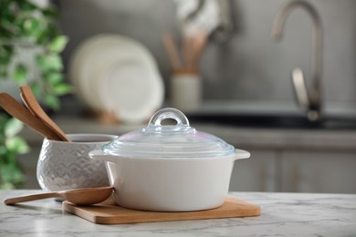 Photo of Ceramic pots and cooking utensils on white marble table in kitchen