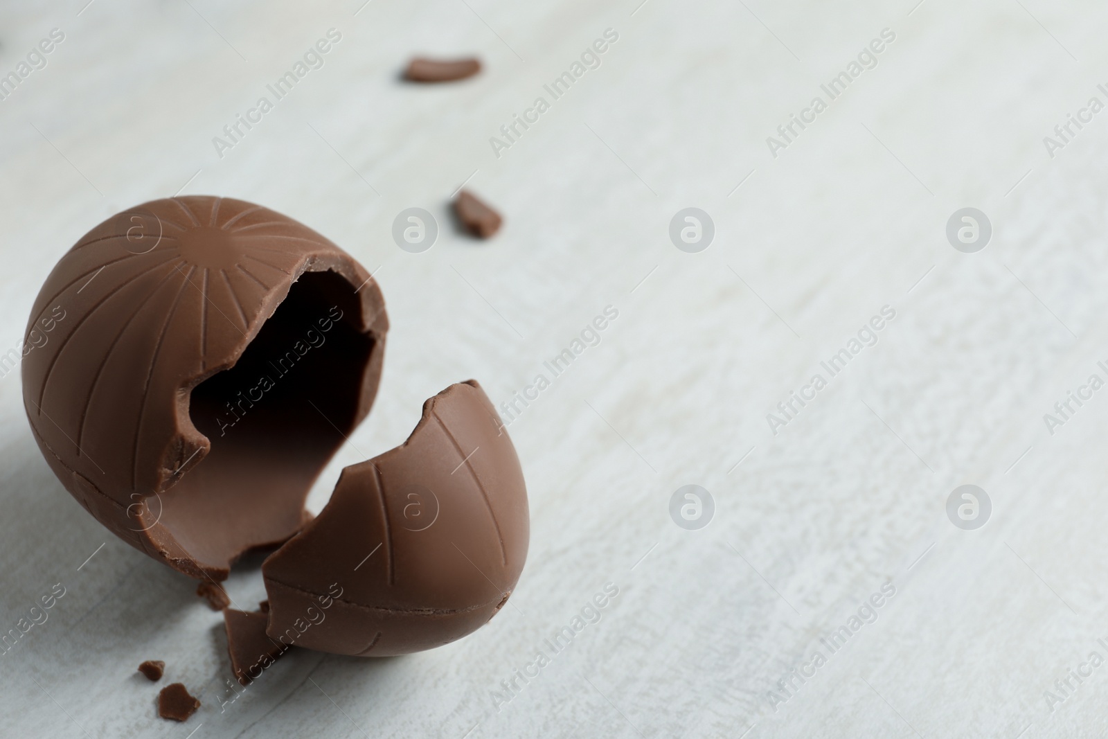 Photo of Broken chocolate egg on white wooden table, closeup. Space for text