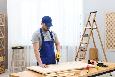 Photo of Young worker using electric drill at table in workshop