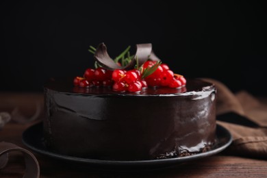 Photo of Tasty homemade chocolate cake with berries and rosemary on wooden table against black background, closeup