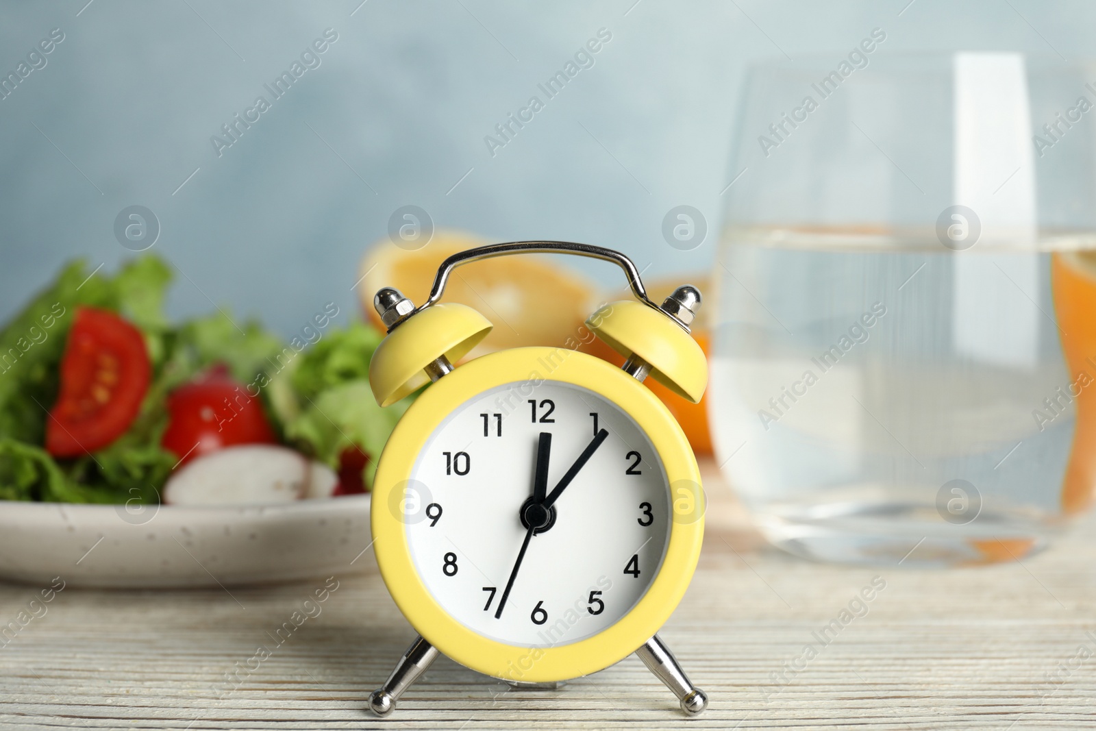 Photo of Alarm clock and healthy food on white wooden table. Meal timing concept