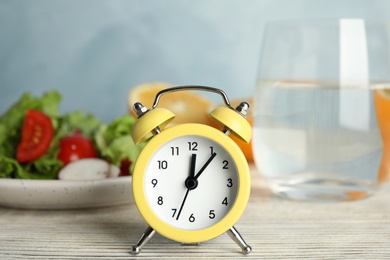 Photo of Alarm clock and healthy food on white wooden table. Meal timing concept