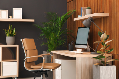 Photo of Comfortable workplace with computer near wooden wall in stylish room interior. Home office design