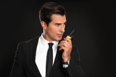 Male security guard in uniform using portable radio transmitter on dark background