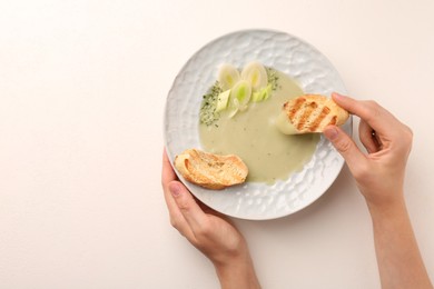 Photo of Woman dipping crouton into delicious leek soup at light table, top view. Space for text