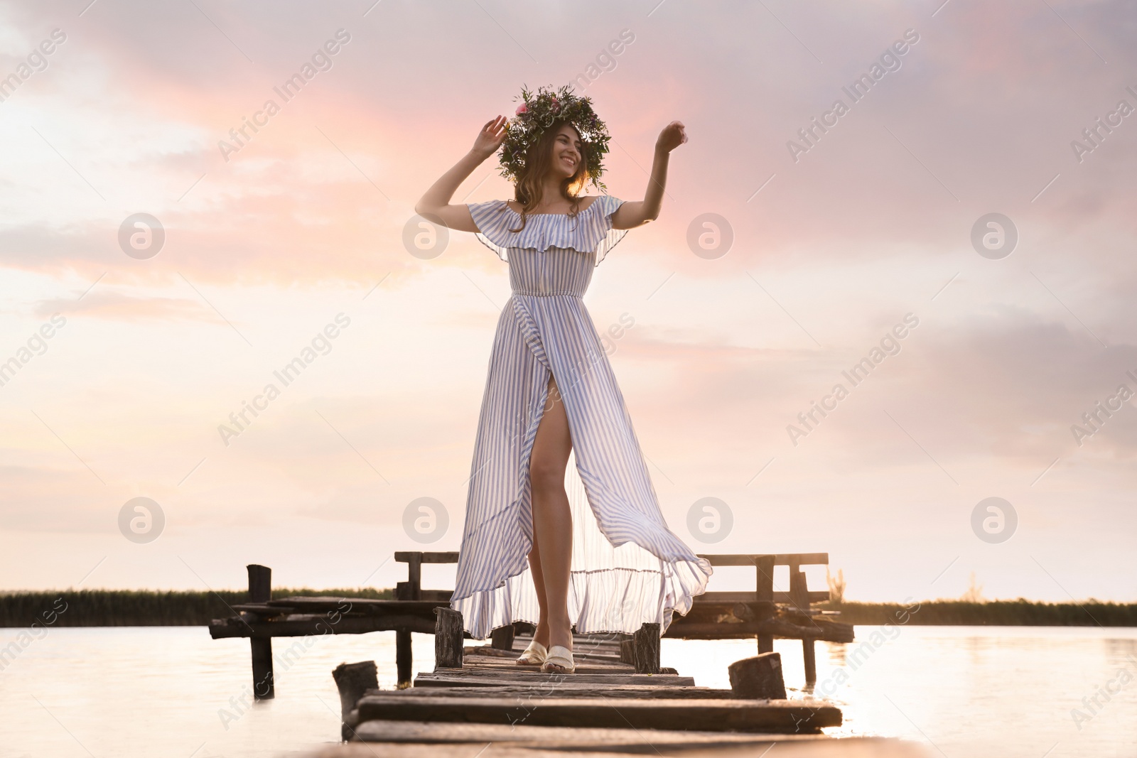 Photo of Young woman wearing wreath made of beautiful flowers on pier near river