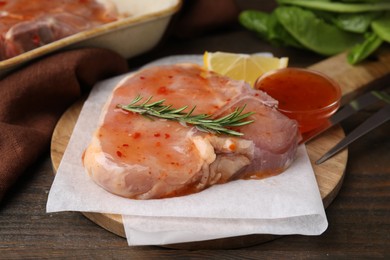 Photo of Board with raw marinated meat and rosemary on wooden table, closeup