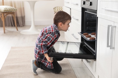 Little boy near open oven with cookies in kitchen