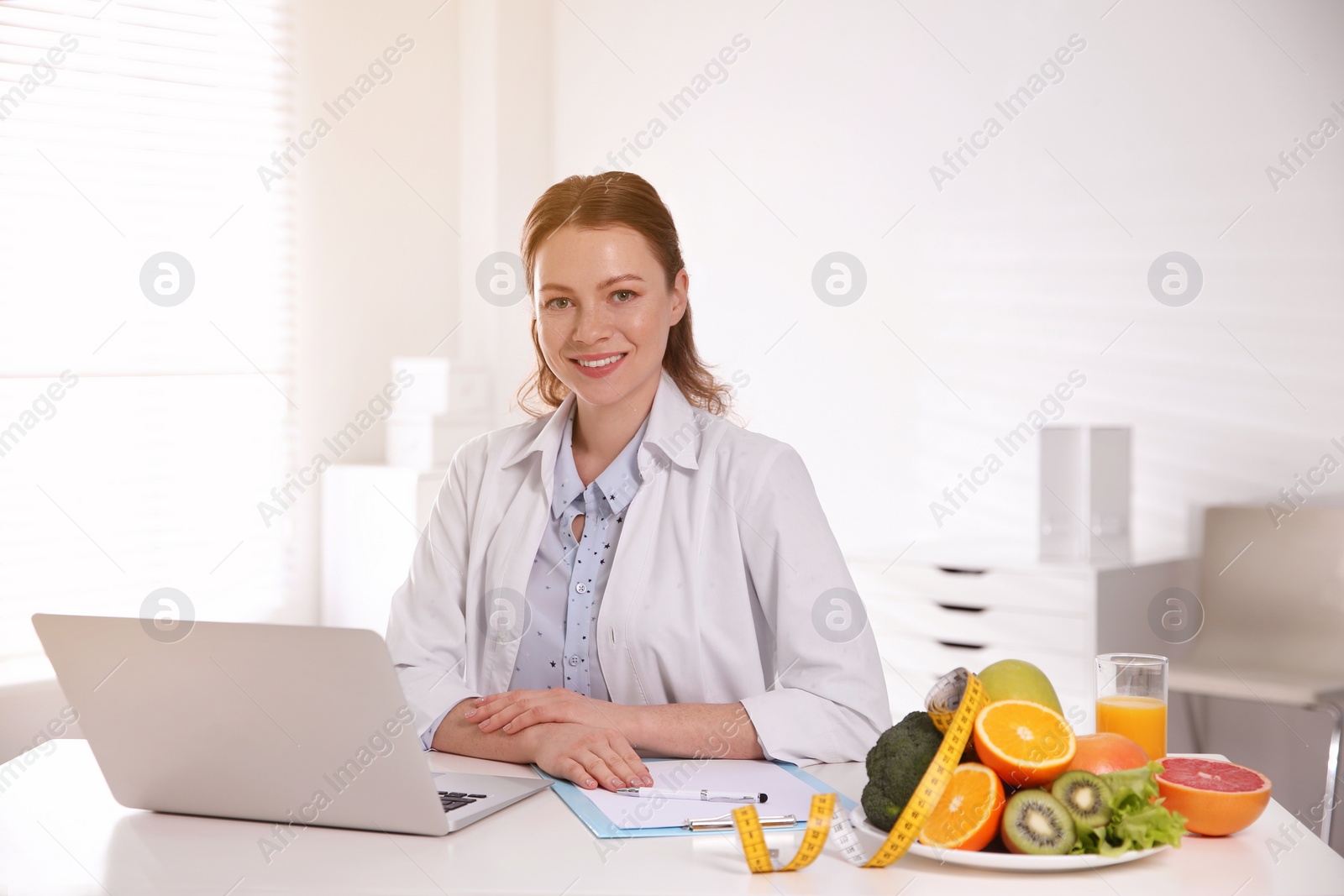 Image of Nutritionist with clipboard and laptop at desk in office