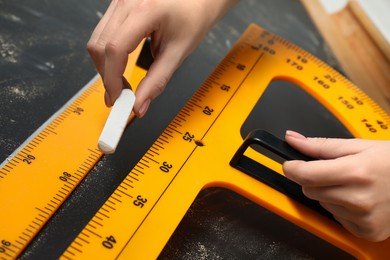 Photo of Woman drawing with chalk, ruler and protractor on blackboard, closeup