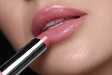 Photo of Closeup view of young woman applying beautiful nude lipstick