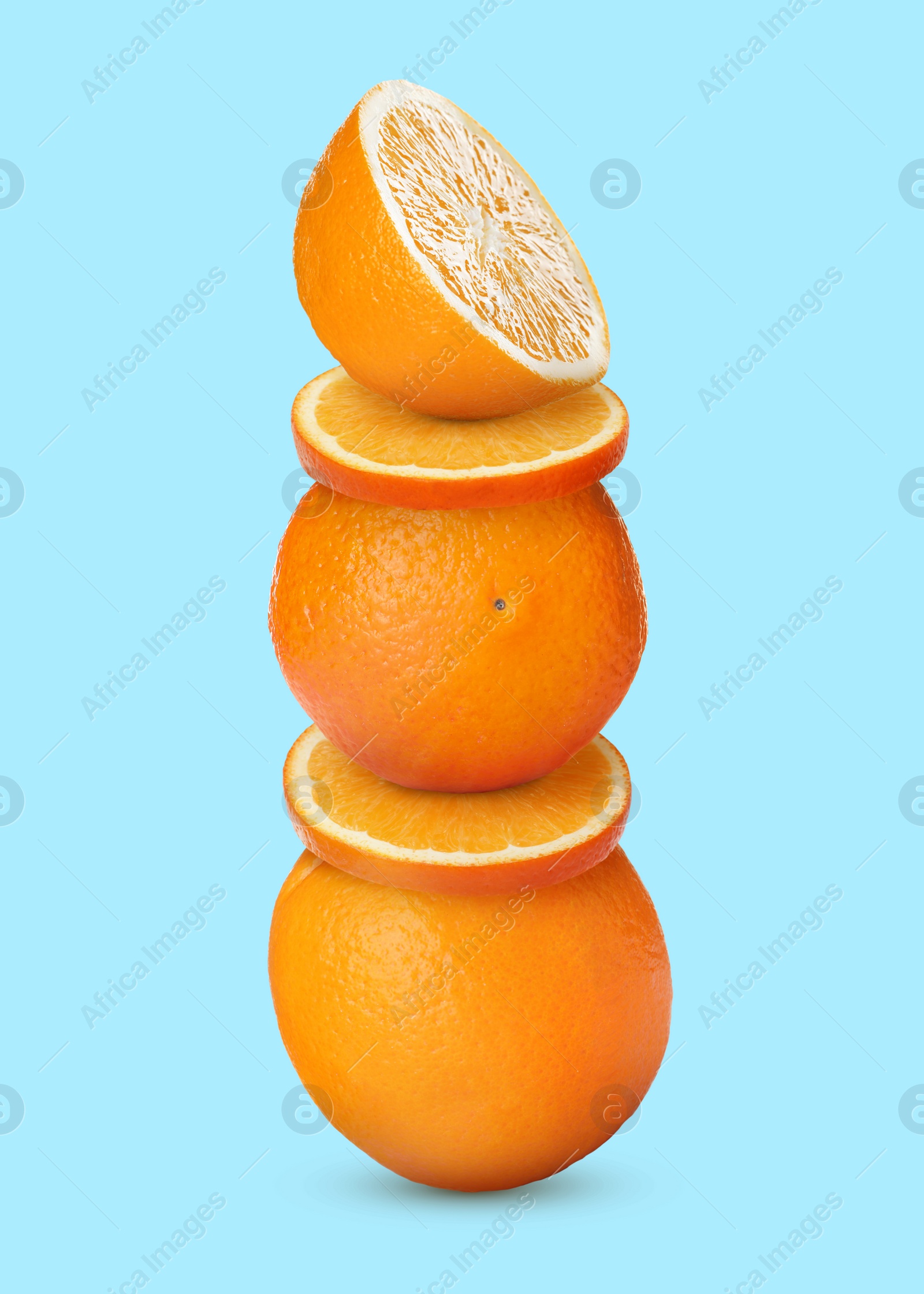 Image of Stacked cut and whole oranges on pale light blue background