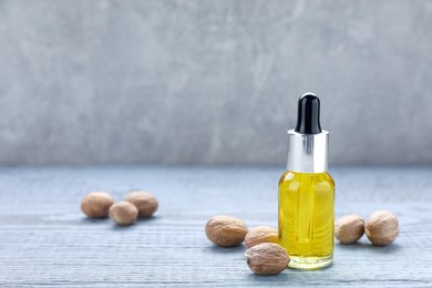 Photo of Bottle of nutmeg oil and nuts on grey wooden table. Space for text