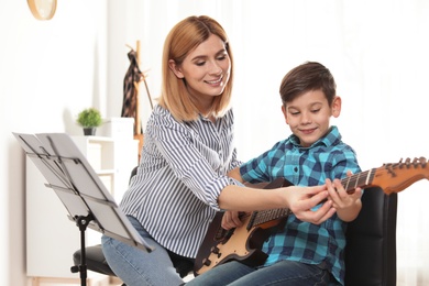 Little boy playing guitar with his teacher at music lesson. Learning notes