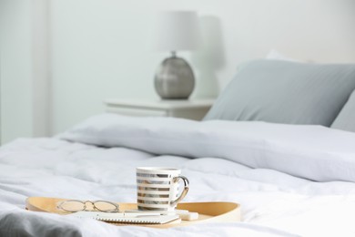 Mug of hot drink with stylish cup coaster, glasses and notebook on bed in room, space for text