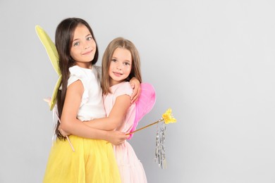 Photo of Cute little girls in fairy costumes with wings and magic wand on light background. Space for text