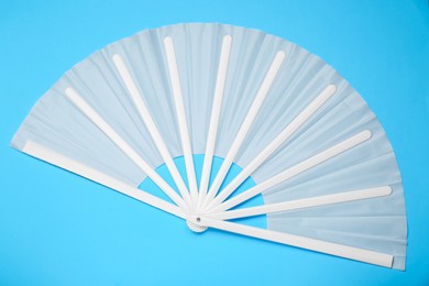 Stylish white hand fan on light blue background, top view